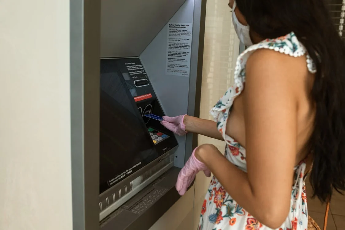 Maszkot viselő nő bankautomatánál kártyát használ, közelről fotózva.